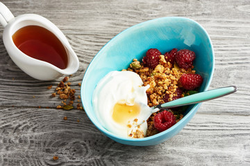 Homemade granola in a bowl with raspberries and maple syrup on a wooden table.