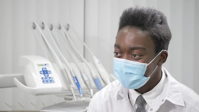 Young African American male doctor dentist in medical mask. Medicine, health, stomatology concept. dentist conducts inspection and concludes