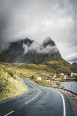 Winding road trip towards Reinebringen in Reine on Lofoten Islands with mountains in the background. Cloudy and moody sky with atlantic ocean. © Mathias
