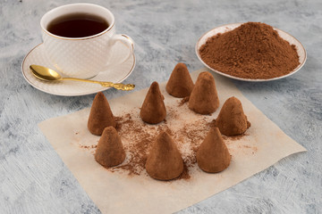 Chocolate candies, cocoa sprinkled, laid on baking paper, a mug of tea.