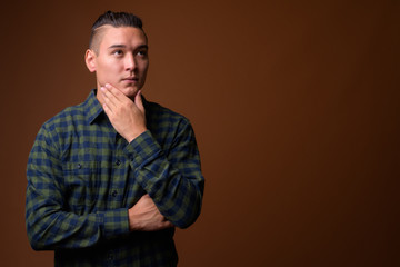 Obraz premium Young handsome multi-ethnic man against brown background