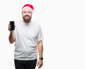 Naklejka premium Young caucasian man wearing christmas hat showing smartphone screen over isolated background with a happy face standing and smiling with a confident smile showing teeth