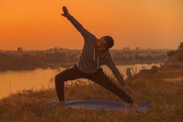 Man doing yoga on sunset with city view.