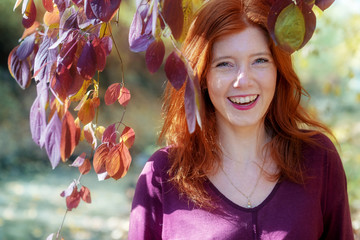 Schönes sexy reizendes junges fuchsiges feuriges rothaariges Mädchen, unter violettem lila Herbst Busch, im Park, mit glücklich, fröhlich, lustig mit Lachen im Gesicht.