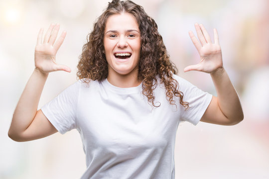 Beautiful brunette curly hair young girl wearing casual t-shirt over isolated background showing and pointing up with fingers number ten while smiling confident and happy.