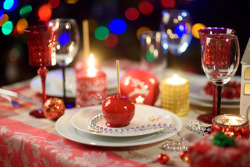 Beautiful table setting for Christmas party or New Year celebration at home. Cozy room with a fireplace and Christmas tree in a background.