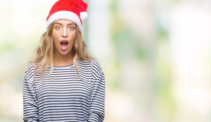 Beautiful young blonde woman wearing christmas hat over isolated background afraid and shocked with...