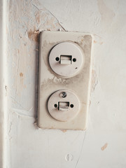 Old and filthy light switch on wall with scratched and scraped off wallpaper during renovation of apartment