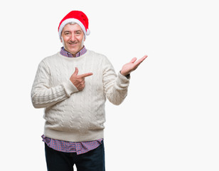 Handsome senior man wearing christmas hat over isolated background amazed and smiling to the camera while presenting with hand and pointing with finger.