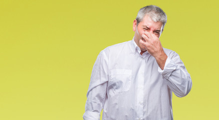 Handsome senior man over isolated background smelling something stinky and disgusting, intolerable smell, holding breath with fingers on nose. Bad smells concept.