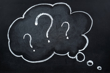 Chalk hand drawing question marks in thought bubble on blackboard 