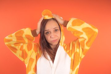 pajamas in the form of a giraffe. emotional portrait of a girl on an orange background. crazy and...