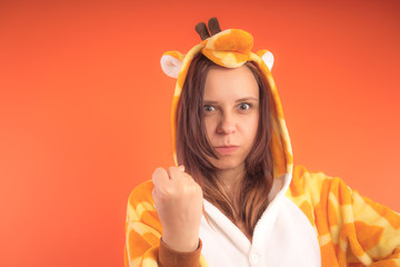 pajamas in the form of a giraffe. emotional portrait of a girl on an orange background. crazy and...
