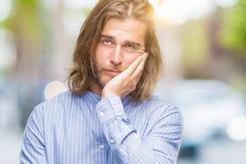 Young handsome man with long hair over isolated background thinking looking tired and bored with depression problems with crossed arms.