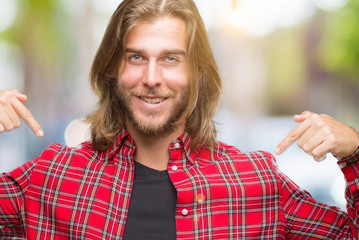Young handsome man with long hair over isolated background looking confident with smile on face,...