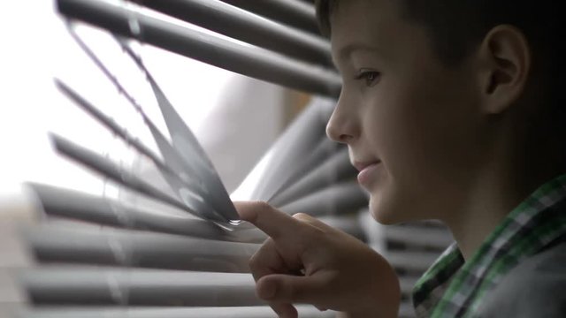 boy looks out the window and waves his hand to someone, says goodbye