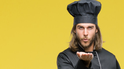 Young handsome cook man with long hair over isolated background looking at the camera blowing a kiss with hand on air being lovely and sexy. Love expression.