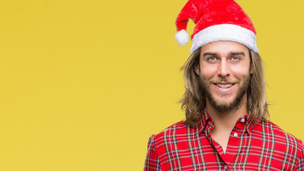 Young handsome man with long hair wearing santa claus hat over isolated background with a happy and cool smile on face. Lucky person.