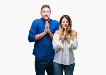 Young couple in love over isolated background praying with hands together asking for forgiveness smiling confident.