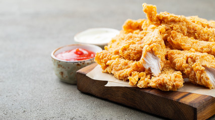 Breaded chicken strips with two kinds of sauces and fried potatoes on a wooden Board. Fast food on...