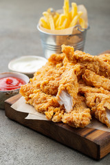 Breaded chicken strips with two kinds of sauces and fried potatoes on a wooden Board. Fast food on dark brown background © Vasiliy