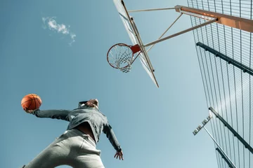 Schilderijen op glas Winning throw. Low angle of a basketball player jumping while doing the winning throw © zinkevych