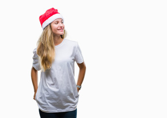Young beautiful blonde woman wearing christmas hat over isolated background looking away to side with smile on face, natural expression. Laughing confident.