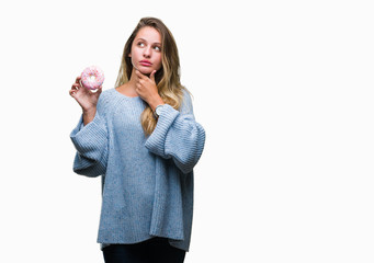Young beautiful blonde woman eating sweet donut over isolated background serious face thinking...