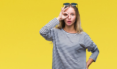 Young beautiful blonde woman wearing sunglasses over isolated background doing ok gesture shocked with surprised face, eye looking through fingers. Unbelieving expression.