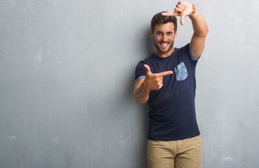 Handsome young man over grey grunge wall smiling making frame with hands and fingers with happy face. Creativity and photography concept.