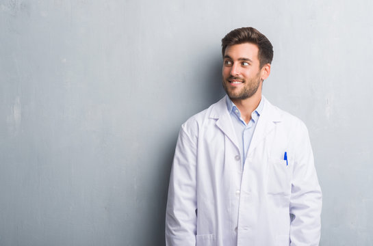 Handsome Young Professional Man Over Grey Grunge Wall Wearing White Coat Smiling Looking Side And Staring Away Thinking.