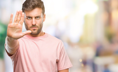 Naklejka premium Young handsome man over isolated background doing stop sing with palm of the hand. Warning expression with negative and serious gesture on the face.