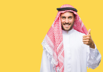 Young handsome man wearing keffiyeh over isolated background doing happy thumbs up gesture with hand. Approving expression looking at the camera with showing success.