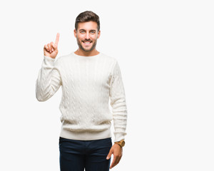 Naklejka premium Young handsome man wearing winter sweater over isolated background showing and pointing up with finger number one while smiling confident and happy.
