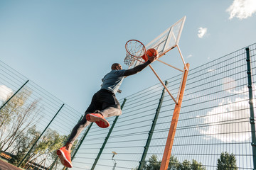 During the training. Nice strong young man jumping up while playing basketball alone