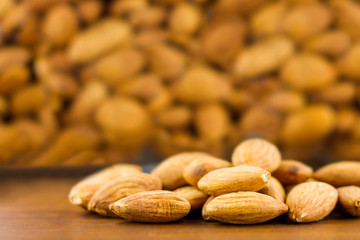 Almonds seeds pour from wood spoon on textured wooden background, top view.
