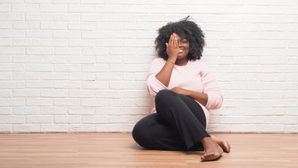 Young african american woman sitting on the floor at home covering one eye with hand with confident smile on face and surprise emotion.