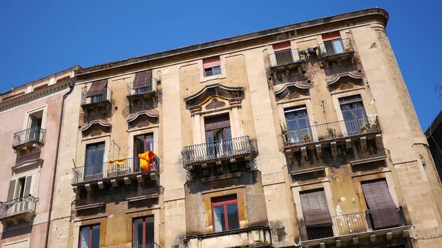 View of balconies and windows on the sunlit facade of a typical mediterranean building in Catania, Sicily.
