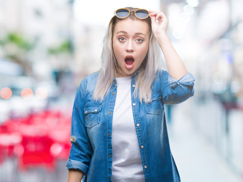 Young blonde woman wearing sunglasses over isolated background afraid and shocked with surprise expression, fear and excited face.