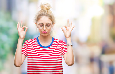 Young beautiful blonde woman wearing glasses over isolated background relax and smiling with eyes closed doing meditation gesture with fingers. Yoga concept.