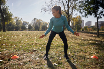one young woman, 20-29 years old, cardio exercise in public park, between two fitness props,  Lateral Shuffle, outdoors, sunny autumn day.