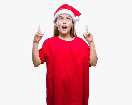 Young beautiful girl wearing christmas hat over isolated background amazed and surprised looking up and pointing with fingers and raised arms.