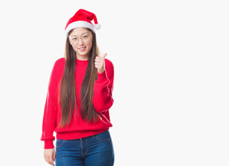 Young Chinese woman over isolated background wearing christmas hat doing happy thumbs up gesture with hand. Approving expression looking at the camera with showing success.