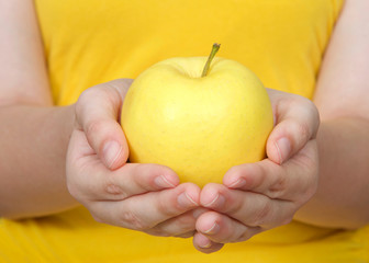 Young female hands holding one golden delicious yellow apple with yellow background.