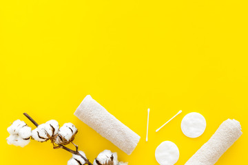 Products made of cotton. Bath accessories. Towels, cotton pads and swabs near dry cotton flowers on yellow background top view copy space