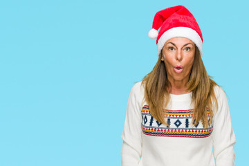 Middle age adult woman wearing winter sweater and chrismat hat over isolated background afraid and shocked with surprise expression, fear and excited face.