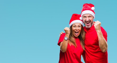 Obraz premium Middle age hispanic couple wearing christmas hat over isolated background very happy and excited doing winner gesture with arms raised, smiling and screaming for success. Celebration concept.