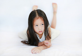 Adorable little Asian girl lying on bed over white background.