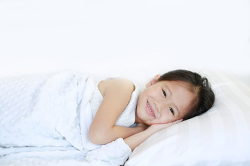 Smiling young Asian kid girl lying on bed.