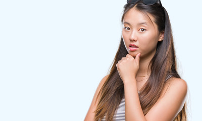 Fototapeta premium Young asian woman wearing sunglasses over isolated background looking confident at the camera with smile with crossed arms and hand raised on chin. Thinking positive.